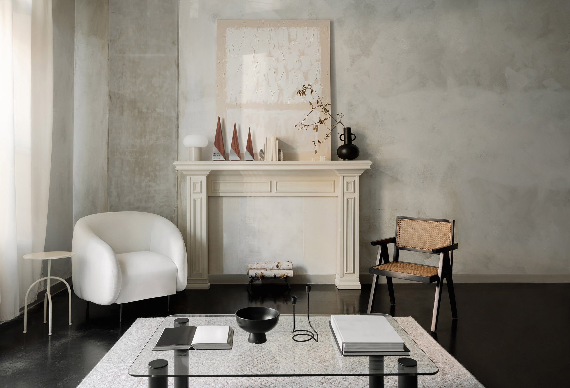 A group of three unique triangular wooden recognition awards sit on a fireplace mantle with a painting behind and a vase with florals next to it. The sophisticated room also has two chairs and a low glass table. 