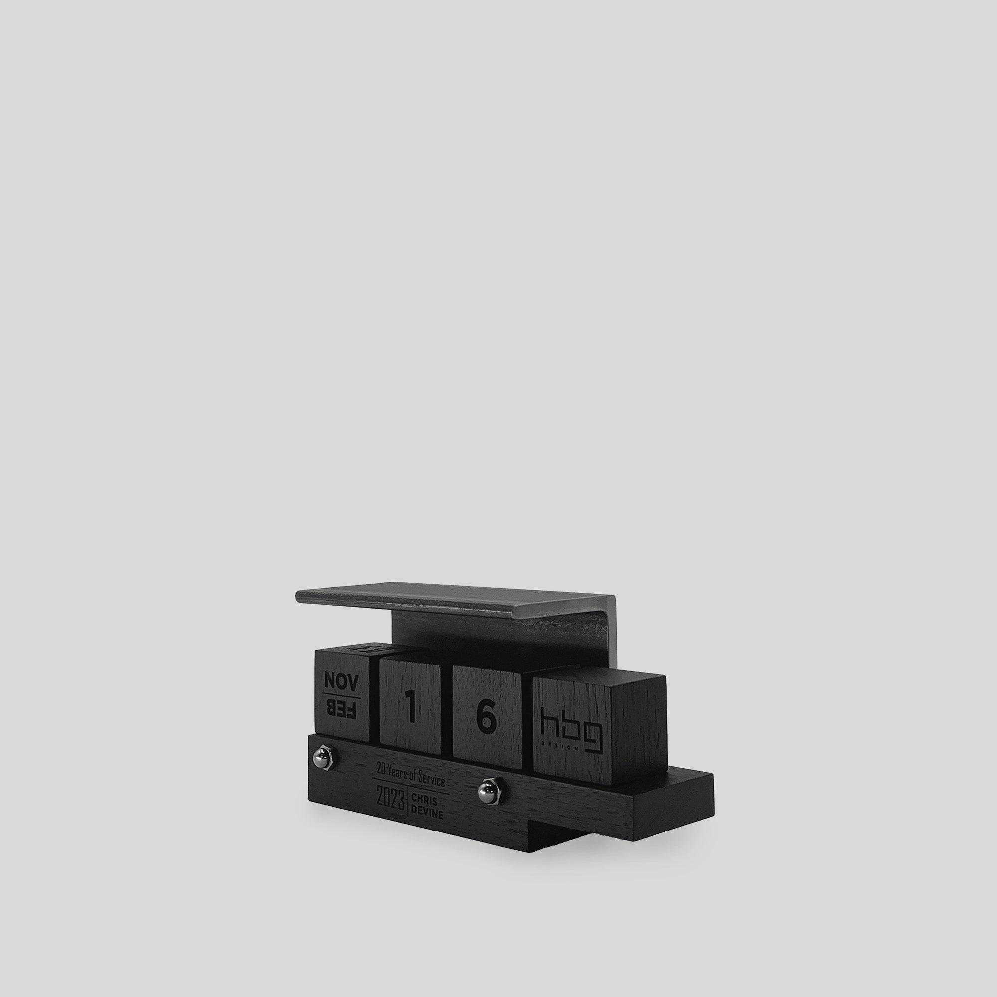 Perpetual Calendar Ferro featuring black wooden blocks with numbers, a steel angle, and a wooden ledge designed for business cards.