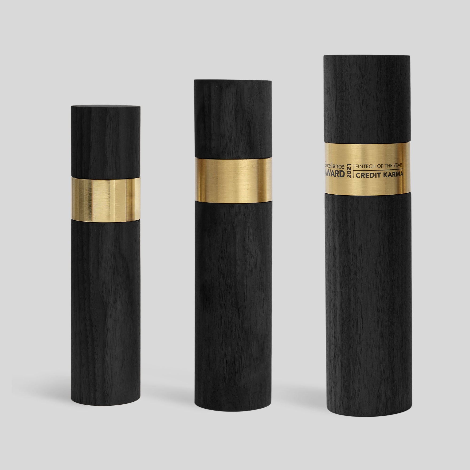 Stela Round Award | Large features black and gold cylinder trophies in three sizes, showcasing a polished metal ring and wood base, symbolizing unity and excellence. Unique, modern, architect-designed and artisan-crafted in USA. 