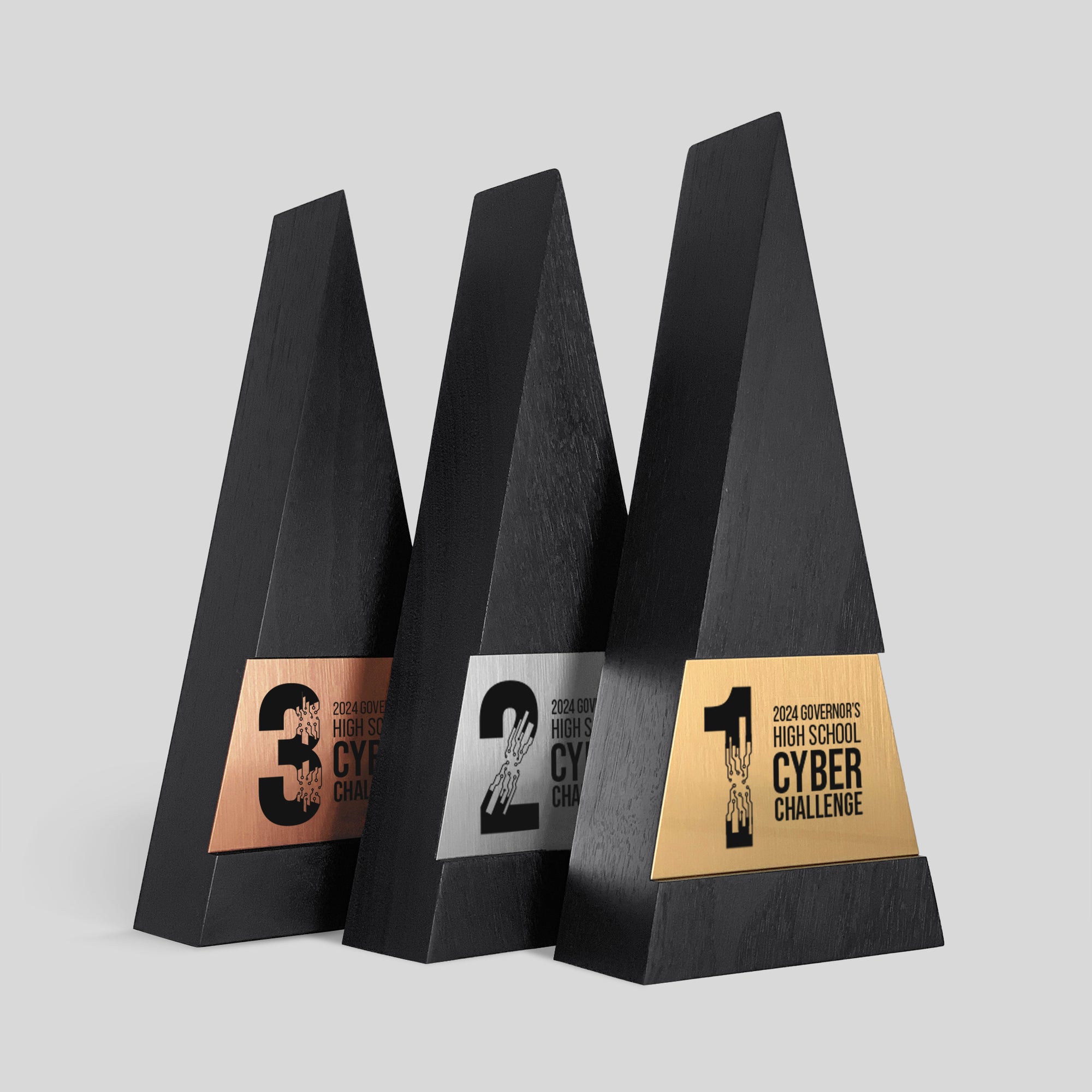 Figura Trigonum Awards featuring black wood and various engraved metal nameplates. Triangle-shaped trophies, symbolizing achievement and ambition. Personalized, elegant, modern, meaningful design.