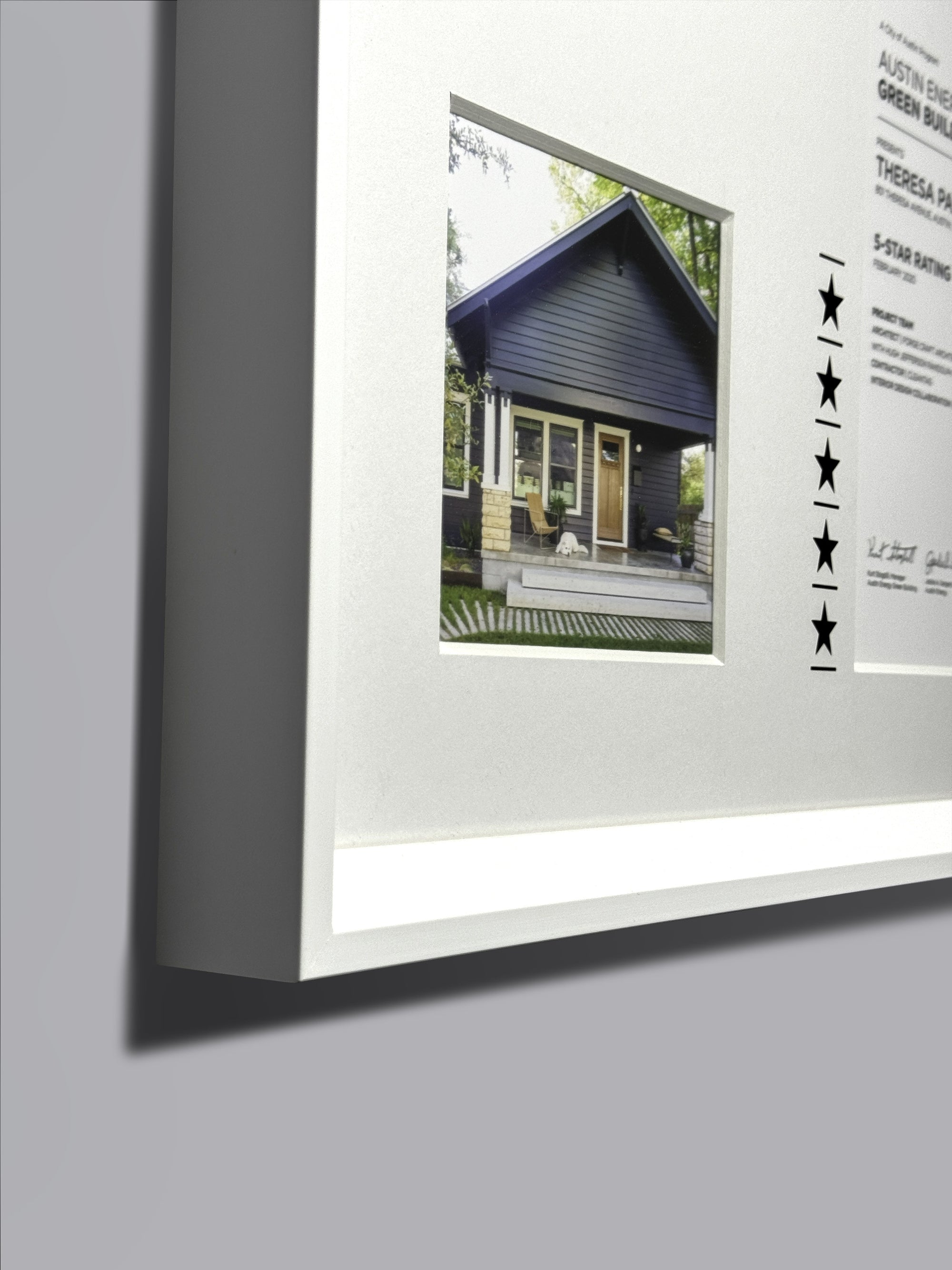 Certificate | White Frame featuring a picture of a house with a front porch, including a chair and window, elegantly displayed within the frame.